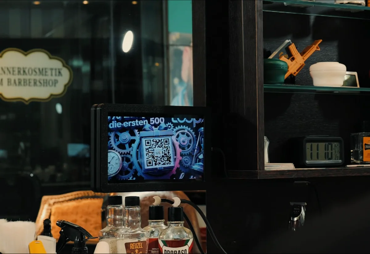 LOOPX13 im Salon: Ein LoopScreen hängt am Spiegel neben dem Regal und zeigt einen Spot, im Sichtfeld vom Stuhl
